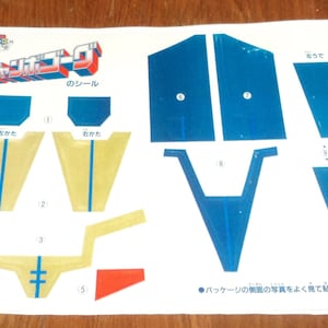 May include: A paper craft template for building a robot. The template includes instructions in Japanese and shows the different pieces needed to build the robot. The pieces are labeled with numbers and include a left wing, right wing, and a body.