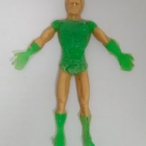 May include: A green and gold plastic action figure of a superhero. The figure has a green suit with a gold belt and boots. The figure has a short, blond hair and a serious expression.