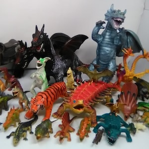 May include: A collection of plastic toy dragons, dinosaurs, and other mythical creatures. The toys are in various colors, including green, red, blue, black, and orange. There is also a gray horse with a saddle.