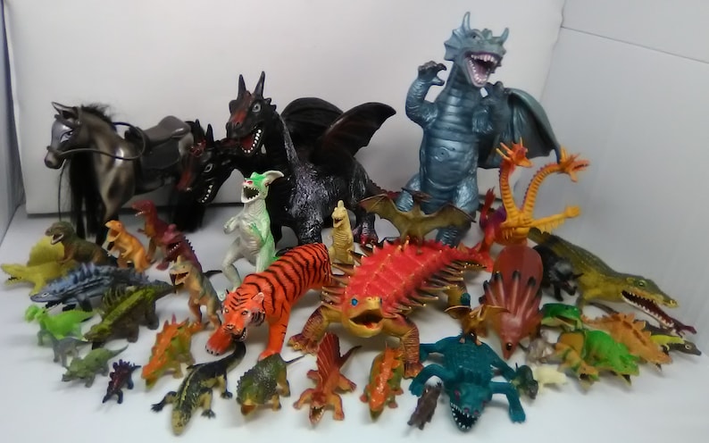 May include: A collection of plastic toy dragons, dinosaurs, and other mythical creatures. The toys are in various colors, including green, red, blue, black, and orange. There is also a gray horse with a saddle.