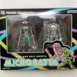 May include: A box containing three action figures. The figures are green, clear, and green and black. The box has the text "RAHIOD Cro-Mannen" and "HALF MAN HALF INSECTA MICRO BATTA" on it. The box is for ages 14 and up.