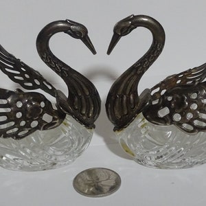 May include: A pair of silver swan salt and pepper shakers with clear glass bases. The swans are facing each other with their necks curved into a heart shape.