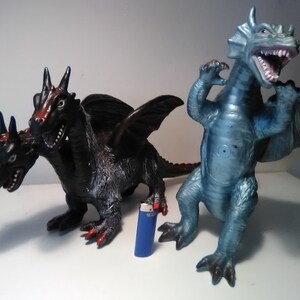 May include: Two plastic toy dragons. One is a three-headed black dragon with red accents. The other is a single-headed blue dragon with a wide open mouth.
