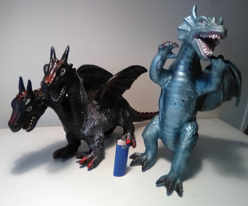 May include: Two plastic toy dragons. One is a three-headed black dragon with red accents. The other is a single-headed blue dragon with a wide open mouth.
