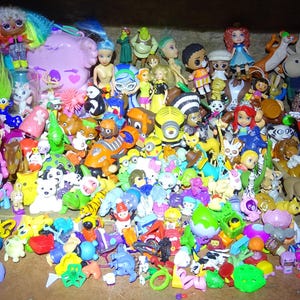 Pode incluir: Uma coleção de várias figuras de brinquedo coloridas, incluindo bonecas, personagens de desenhos animados e animais. Os brinquedos estão dispostos em um recipiente de madeira, mostrando uma variedade de tamanhos e designs. O sortimento inclui personagens populares e itens colecionáveis.