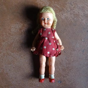 Puede incluir: Muñeca vintage con cabello rubio y ojos azules, vestida con un vestido rojo con lunares blancos. La muñeca tiene zapatos rojos y calcetines blancos. Un juguete clásico.