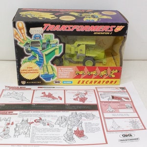 May include: A green and yellow Transformers Excavator toy robot in its vehicle form. The box features the text "Transformers Generation 2" and "Excavator". The toy comes with instructions and a missile launcher.