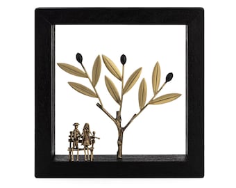 May include: A black framed wall decor featuring a gold metal olive tree with black olives and a couple sitting on a bench beneath the tree.