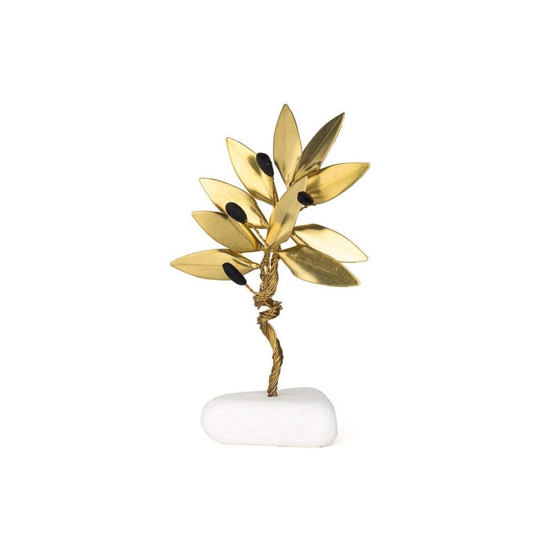 May include: A decorative gold-colored metal olive branch sculpture with black accents. The leaves are a shiny gold, and the olives are black. The sculpture is mounted on a small, white, rectangular stone base.