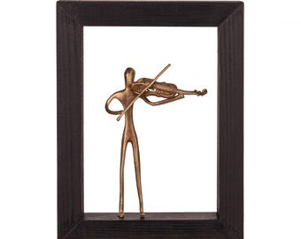 May include: A gold-toned metal sculpture of a person playing a violin, framed in a black wood frame.
