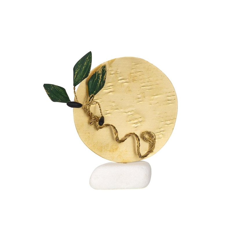 May include: A decorative sculpture featuring a textured gold-colored disc with a green and gold leaf design and a twisted gold-colored wire. The sculpture is balanced on a white stone base. The leaves have a dark green and gold pattern.