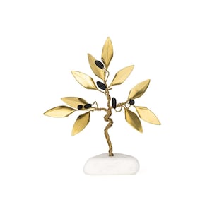 May include: A decorative brass tree sculpture with gold-colored leaves and black accents. The tree is mounted on a white stone base, creating a natural and elegant aesthetic. The leaves are shaped like olive leaves.
