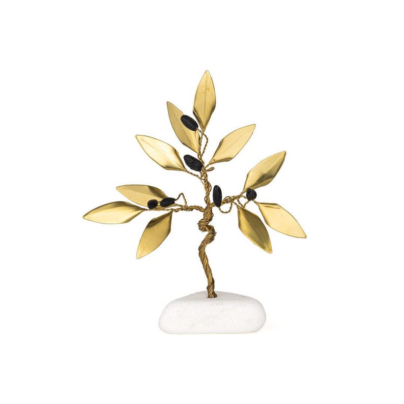 May include: A decorative brass tree sculpture with gold-colored leaves and black accents. The tree is mounted on a white stone base, creating a natural and elegant aesthetic. The leaves are shaped like olive leaves.