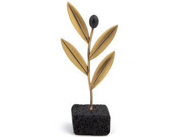 May include: A gold metal olive branch sculpture with a black olive on the stem. The sculpture is mounted on a black lava rock base.