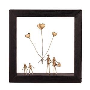 Könnte beinhalten: Ein quadratischer schwarzer Holzrahmen mit einer bronzefarbenen Metallskulptur einer vierköpfigen Familie. Zwei Erwachsene und zwei Kinder stehen darin, wobei die Erwachsenen drei herzförmige Luftballons an dünnen Drähten halten.