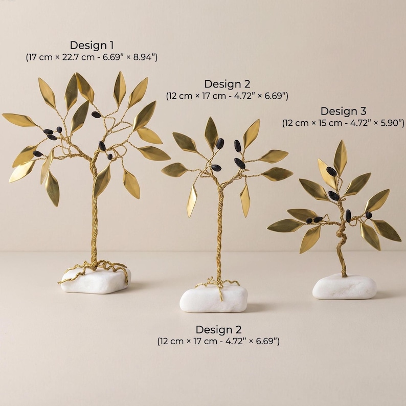 May include: Three decorative golden metal tree sculptures with leaf and berry details, each mounted on a white stone base. Design 1 measures 6.69" x 8.94", Design 2 measures 4.72" x 6.69", and Design 3 measures 4.72" x 5.90".