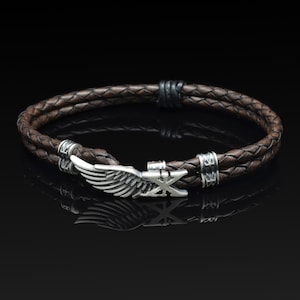 Op de afbeelding: Een bruin leren armband met een zilveren vleugel en een zilveren sluiting. De armband is gevlochten en heeft een zilveren accent op de sluiting.