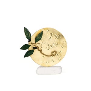 May include: A decorative sculpture featuring a gold-colored, textured circular element with a green and black leaf and stem design. The sculpture is mounted on a white, rectangular base. The overall design is artistic and nature-inspired.