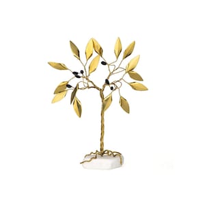 May include: A decorative gold-colored metal tree sculpture with gold leaves and black berry accents. The tree is mounted on a white stone base. The sculpture is a decorative home accent.