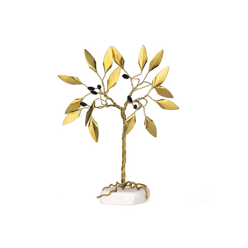 May include: A decorative gold-colored metal tree sculpture with gold leaves and black berry accents. The tree is mounted on a white stone base. The sculpture is a decorative home accent.