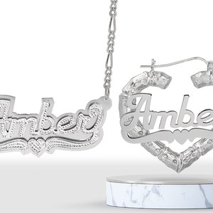 May include: Silver necklace and hoop earrings with the name "Amber" in a cursive font with a heart design.