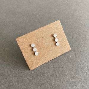 May include: A pair of silver earrings with a row of four small, round discs on each earring.