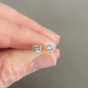 May include: A pair of silver heart-shaped stud earrings with clear cubic zirconia stones.