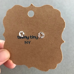 May include: A pair of silver hammered circle stud earrings on a brown card with the text "teeny tiny NY".