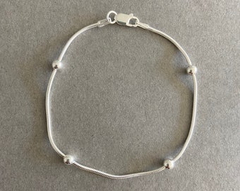 Puede incluir: Un brazalete de cadena de plata con cuatro pequeñas cuentas redondas.
