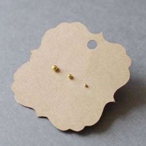 May include: Three gold-colored stud earrings of different sizes on a brown paper card.