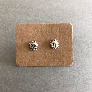 Könnte beinhalten: Ein Paar silberne Ohrstecker mit einem Sonnendesign. Die Sonne hat ein Gesicht mit einem Lächeln.