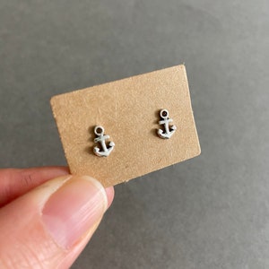 May include: A pair of silver anchor earrings on a brown card.