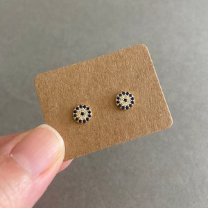 May include: A pair of gold earrings with a blue and white evil eye design. The earrings are small and delicate.