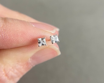 May include: A pair of silver stud earrings with small square-shaped clear cubic zirconia stones.