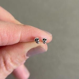 Op de afbeelding: Een paar zilveren schedel oorbel studs met zwarte email details.