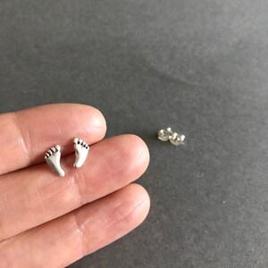May include: A pair of silver stud earrings shaped like tiny footprints.