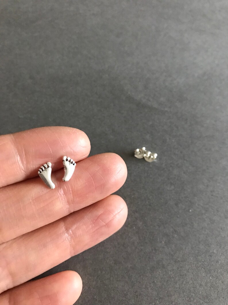 May include: A pair of silver stud earrings shaped like tiny footprints.