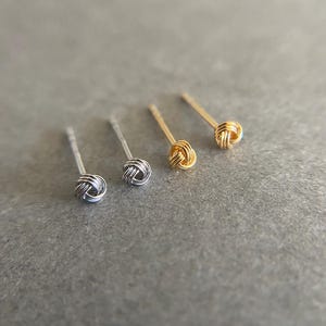 May include: Three pairs of knot-style earrings in silver and gold. The earrings are small and delicate.
