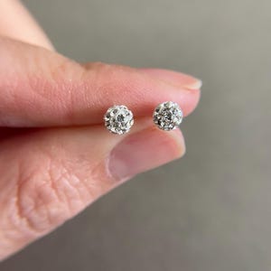 Puede incluir: Un par de pendientes de botón de plata con pequeños acentos de cristal redondos y transparentes.