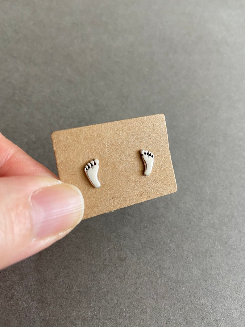 May include: A pair of silver stud earrings shaped like footprints.