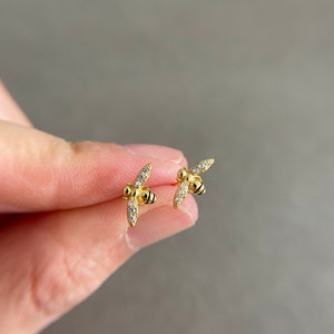 May include: A pair of gold bee stud earrings with clear crystal accents.