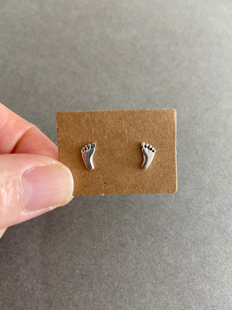 May include: A pair of silver stud earrings shaped like footprints.