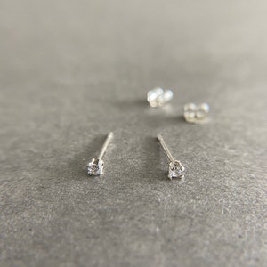 May include: A pair of silver stud earrings with small clear cubic zirconia stones.