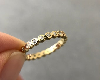 Pode incluir: Um anel de banda de ouro com uma fileira de pequenas pedras preciosas redondas e transparentes.