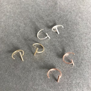 May include: Five nose rings in different colors: silver, gold, rose gold. Each ring has a small, straight bar attached to the hoop.