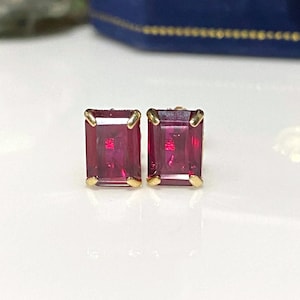 Può includere: Un paio di orecchini d'oro con pietre preziose rosse a taglio smeraldo.