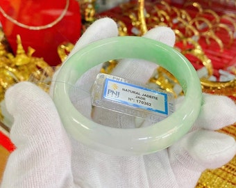 May include: A green jadeite jade bangle bracelet with a white tag that reads "NATURAL JADEITE JADE N°: 170362".
