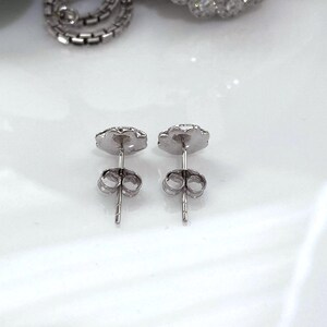 Puede incluir: Un par de pendientes de plata con un dise&ntilde;o floral. Los pendientes tienen un cierre de poste y mariposa. Los pendientes est&aacute;n sobre una superficie blanca.