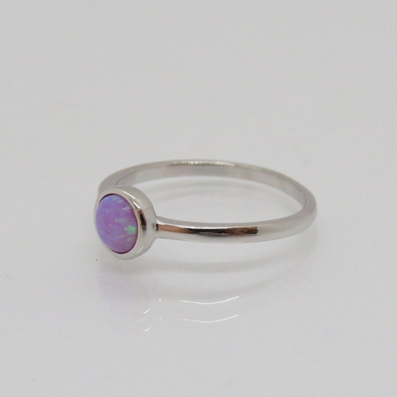 Puede incluir: Un anillo de plata con una piedra de &oacute;palo redonda, de color lila claro. El &oacute;palo tiene un sutil juego de colores. La banda del anillo es delgada y pulida, creando un dise&ntilde;o minimalista. El anillo est&aacute; sobre un fondo blanco.