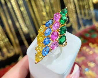 May include: A gold ring with a cascading design of colorful gemstones. The ring features a row of emerald green stones, followed by pink, blue, and yellow stones.